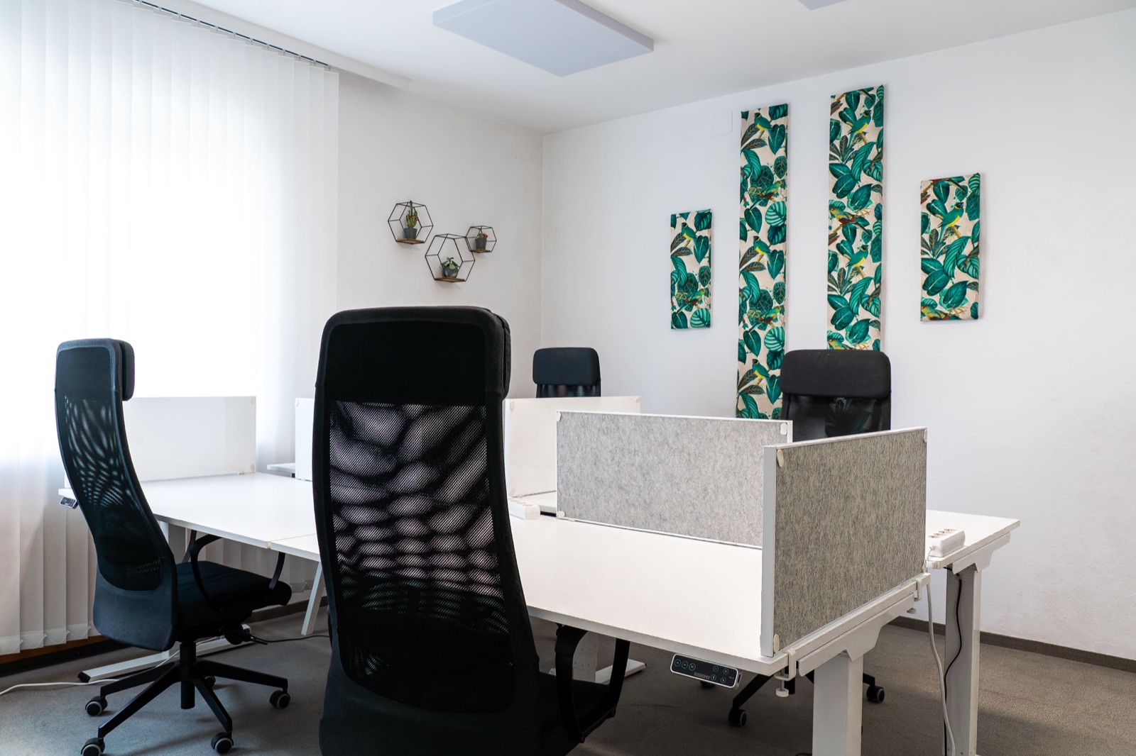 Coworking Bereich mit höhenverstellbaren Schreibtischen und botanischem Wanddekor